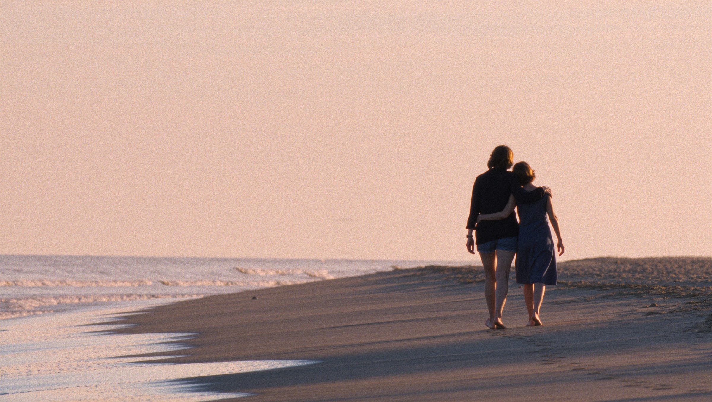 Two women walking along a beach at golden hour